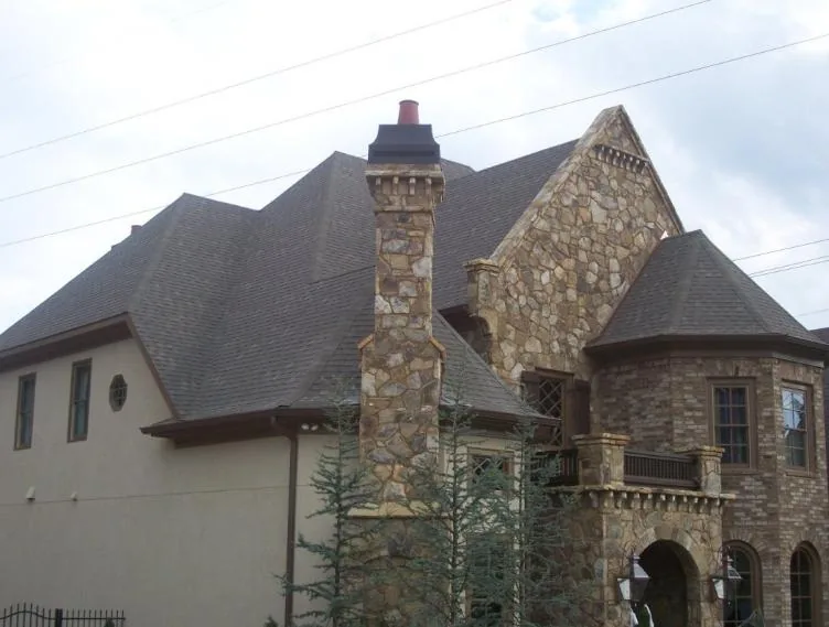 A large stone-and-brick Atlanta home with a tall natural-stone chimney against the sky