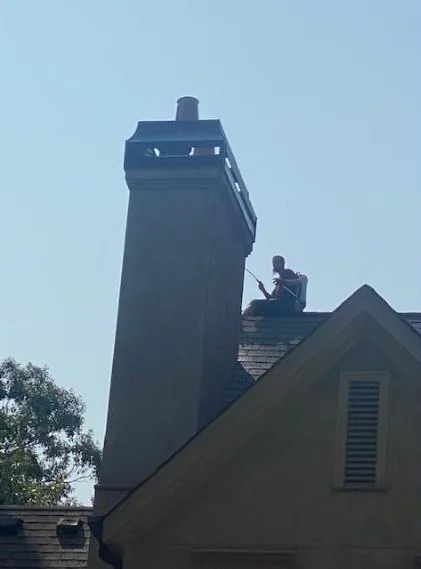 A chimney technician working on a rooftop chimney against a clear blue sky